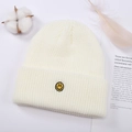 Detalle de textura de punto de gorro crema con bordado de carita sonriente amarilla y algodón - Talla única / Blanco