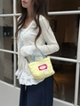 Detail of yellow quilted mini crossbody bag with denim handles on a white cardigan - Yellow