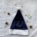 Flat lay detail of a navy blue plush Santa hat with a white pompom and pinecone decor - Navy Blue Plush Hat