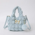 Detalle de bolso de nylon plisado azul claro con lazo dorado y pompón de peluche suave - Azul