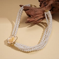 Détail d'un collier de perles multicouche avec pendentif fleur dorée sur une branche de bois - Style Court Multicouches Blanc (47cm)