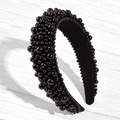 Dettaglio del cerchietto nero largo con perle lucide su una superficie di legno strutturata - Nero