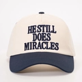 Detail of embroidered HE STILL DOES MIRACLES text on a navy and cream baseball cap - Cream/Navy Blue