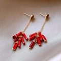 Eleganti orecchini dorati con pendenti a nappa rossi su sfondo di tessuto grigio chiaro - Stile Nappa Petardo Tondo Rosso