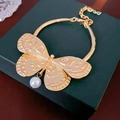 Close-up of golden butterfly pendant with textured wings and white pearl drop on jewelry box - Butterfly Pearl Style / Gold