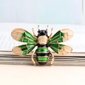 Cartoon honey bee brooch with green enamel wings and gold alloy finish on a book - Bee / Green