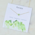 Golden cross chain necklace with a natural green Peridot crystal on a marble background - Peridot