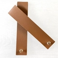 Detail of two brown PU leather straps with metal rivet fasteners on a wood background - Folded Size 15x3cm / Brown