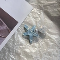 Detalle de horquilla con estrella de mar azul, perla y concha sobre papel texturizado - Azul