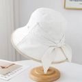 Detalle de sombrero tipo bucket crema con lazo grande, botón de metal y tela tejida - Blanco