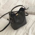 Petit sac seau noir en cuir avec bandoulière et détails dorés sur des draps blancs doux - Noir
