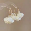 Detalle de pendientes de aro dorados con pétalos de tela blanca y perlas elegantes - Blanco