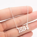 Close-up of a silver 1984 birth year pendant necklace held to show delicate chain detail - 1984 / Steel