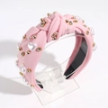 Pink knotted headband featuring heart-shaped pearls and rhinestones on a display stand - Light Pink