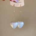 Detail of white pearl heart earrings with golden hooks on a display card held by hand - White