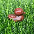Hand-carved red natural stone duck figurine placed on a lush green lawn background - Red Sesame