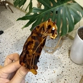 Close-up of amber leopard print hair claw clip held in hand showing tortoiseshell texture - Standing Dark Tortoiseshell Leopard