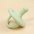 Close-up of light green silicone baby pacifier with textured handle on beige background - Cyan