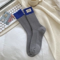 Grey knitted wool socks with blue ribbed cuffs and woven label on white bedding - One Size / 452 Gray