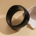 Nahaufnahme eines breiten schwarzen Acryl-Armreifs mit Hochglanz-Finish auf minimalistischem Stein - Schwarzer Unregelmäßiger Stil