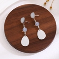 Detailed view of translucent water drop tassel earrings on a dark wooden plate - E3072-2/Translucent White Drop
