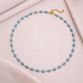 Detailed shot of golden evil eye necklace with blue beads on soft pink fabric background - Lake Blue