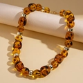 Dettaglio di perline in acrilico ambrato con distanziali dorati e trama a guscio di tartaruga - Stile Geometrico Ambra (Collana-Geometrico Marrone)