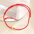 Détail d'un bracelet tressé rouge avec cœur doré sur une colonne et reflet miroir - Rouge