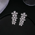 Detailed view of silver metallic triple flower drop earrings on a black textured surface - Silver Triple Flower Eardrops (S3102)