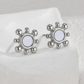 Pendientes de sol minimalistas en plata con centro blanco sobre fondo con textura - Color Acero