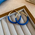 Dettaglio di orecchini a cerchio dorati con smalto blu Klein in una scatola portagioie - Perno in Argento - Combinazione Oro e Blu