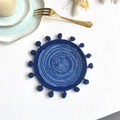 Handwoven round blue cotton coaster with decorative pom-poms on a white table setting - 13cm Coaster / Blue