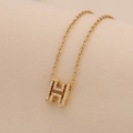 Close-up of a gold O-chain necklace featuring a glittering crystal-encrusted H-pendant - Letter H