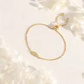 Detailed view of a gold wing pendant bracelet with cubic zirconia on a textured background - Wing