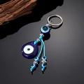 Ethnic blue evil eye keychain with glass beads and tassels on a black reflective surface - Teardrop Glass Eye
