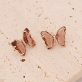 Macro detail of butterfly stud earrings with rose gold base and amber brown wings - Coffee
