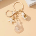 Detalle de llavero dorado con estrella de mar, caracola y colgantes de resina - Blanco Luminoso