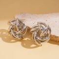 Macro view of silver geometric hollow flower knot stud earrings on a stone base - Silver