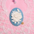 Close-up of oval blue resin cameo with white rose relief on pink lace background - Lake Blue Base White Flower