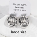 Detail of large silver twisted knot copper earrings on textured white pedestal - Large / White Gold