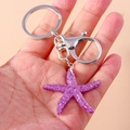 Detailed view of a purple glitter starfish keychain held in hand with silver lobster clasp - Purple Starfish