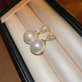 Close-up of gold drop earrings with large white pearl and pavé-set gemstones on cushions - Gold