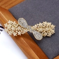 Elegant gold bow hair clip with pearls and rhinestones on a wooden tray display - Pearl Ribbon