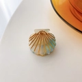 Close-up of shell-shaped acetate hair claw with pearlescent finish and gold accents - Light Blue