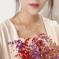 Elegante collar de oro con perlas naturales blancas llevado por una modelo sobre fondo de flores - Estilo de Perlas de Tamaños Mixtos