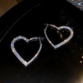 Primer plano de aretes de corazón plateados con cristales blancos sobre un fondo negro - Estilo de Aro con Corazón de Diamantes de Imitación / Plateado