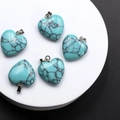 Set of five heart-shaped turquoise stone pendants with metal rings on white pedestal - Synthetic Turquoise