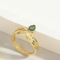 Dettaglio anello avvolgente dorato strutturato con gemma verde su superficie in pietra - Goccia d'Acqua Zircone Verde