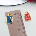 Ethnic alloy pendants in blue and red with gold characters next to a measuring ruler - Red Blue Bright Gold Shun Fu Tag (22801)