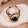 Dettaglio di un bracciale geometrico dorato con corda nera e gemma ovale incastonata - Bracciale / Oro